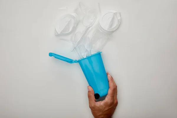 Vue recadrée de l'homme tenant la corbeille bleue avec des tasses en plastique froissées sur fond blanc — Photo de stock