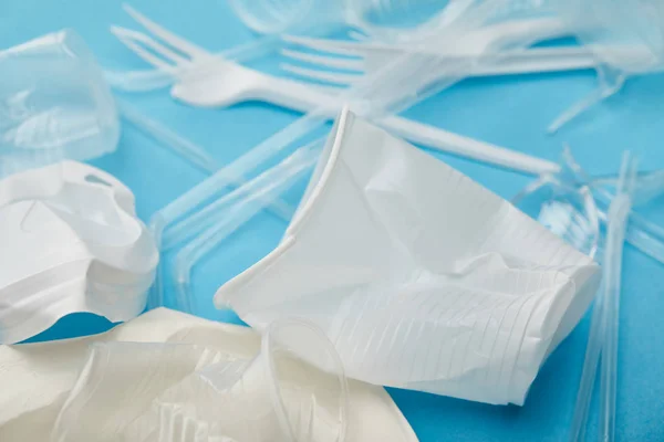 Copos de plástico branco e transparente amassado e garfos no fundo azul — Fotografia de Stock