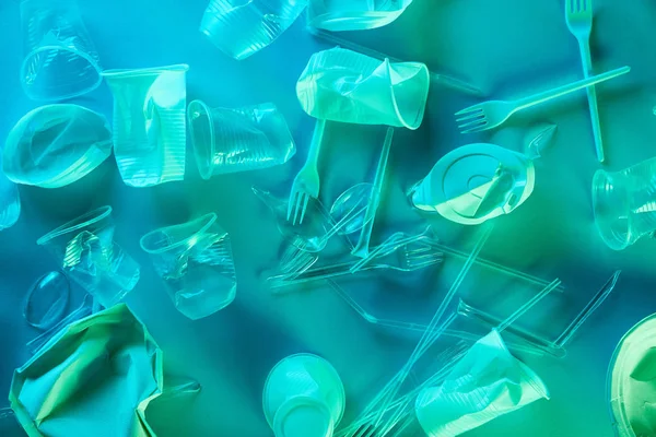 Vista superior de copas de plástico arrugado, pajitas y tenedores en luz azul - foto de stock
