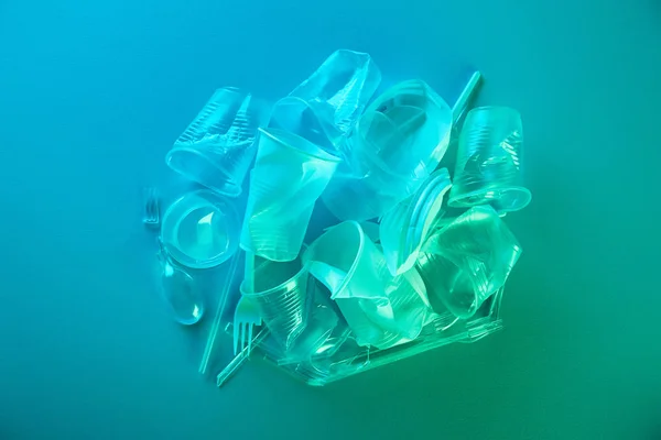 Vista superior de la pila de bolsas de plástico arrugado, tazas, pajitas y tenedores con espacio para copiar en luz azul - foto de stock