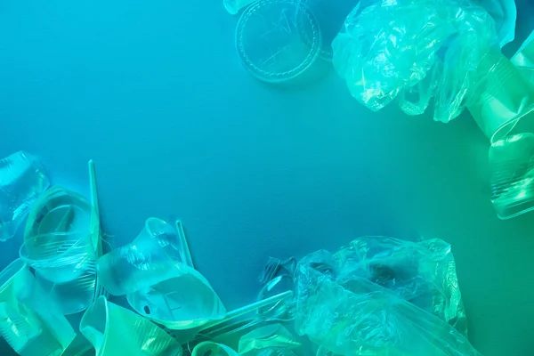 Vista superior de bolsas de plástico arrugadas, tazas, pajitas y tenedores en luz azul - foto de stock
