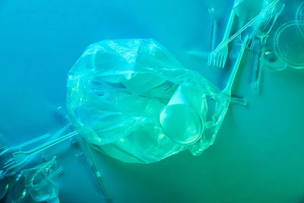 Vue de dessus du sac en plastique froissé, des tasses et des fourchettes en lumière bleue — Photo de stock