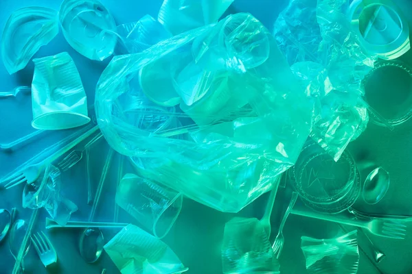 Vista superior de bolsas de plástico arrugado y tazas en luz azul - foto de stock