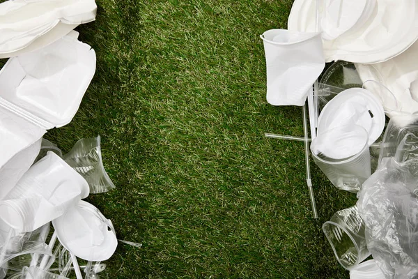 Вид зверху на збиті пластикові чашки та тарілки на траві з копіювальним простором — стокове фото