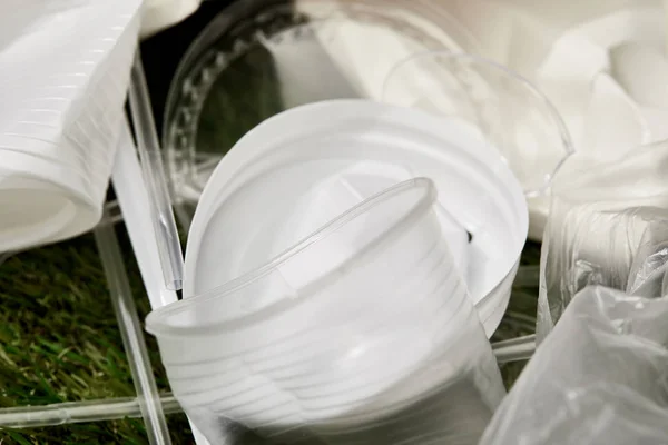 Близкий вид скомканных белых и прозрачных пластиковых чашек на траве — стоковое фото