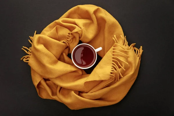 Vue du dessus du thé en tasse dans une écharpe confortable sur fond noir — Photo de stock