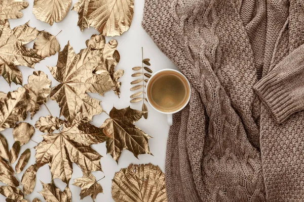 Draufsicht auf gestrickten braunen Pullover, Kaffee und goldenes Laub auf weißem Hintergrund — Stockfoto