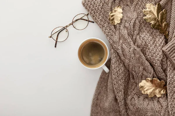 Draufsicht auf gestrickten braunen Pullover, Brille, Kaffee und goldenes Laub auf weißem Hintergrund — Stockfoto