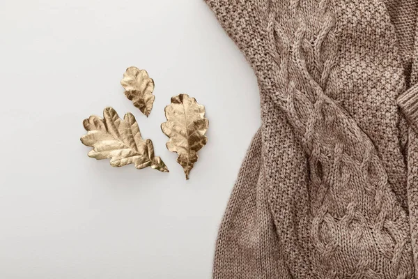 Draufsicht auf gestrickten braunen Pullover und goldene Blätter auf weißem Hintergrund — Stockfoto