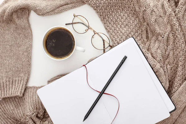 Draufsicht auf leeres Notizbuch, gestrickten braunen Pullover, Kaffee und Gläser auf weißem Hintergrund — Stockfoto