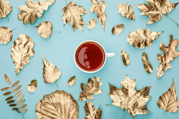 Draufsicht auf Tee im Becher nahe goldenem Laub auf blauem Hintergrund — Stockfoto