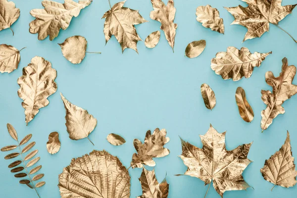 Vista superior de hojas doradas otoñales pintadas sobre fondo azul - foto de stock