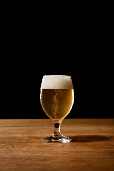 Vaso de cerveza con espuma blanca sobre mesa de madera aislada sobre negro - foto de stock
