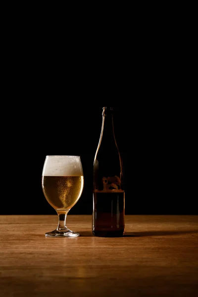 Vaso y botella de cerveza sobre mesa de madera aislada sobre negro - foto de stock