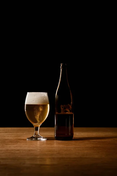 Verre et bouteille de bière sur table en bois isolé sur noir — Photo de stock