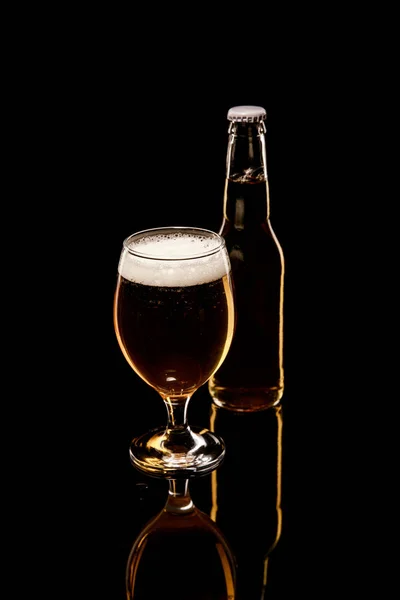 Botella y vaso de cerveza con espuma blanca y burbujas aisladas en negro - foto de stock