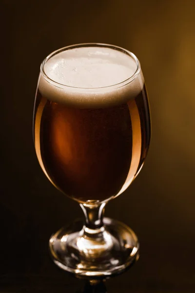 Close up view of beer with foam in glass on dark background with lighting — Stock Photo