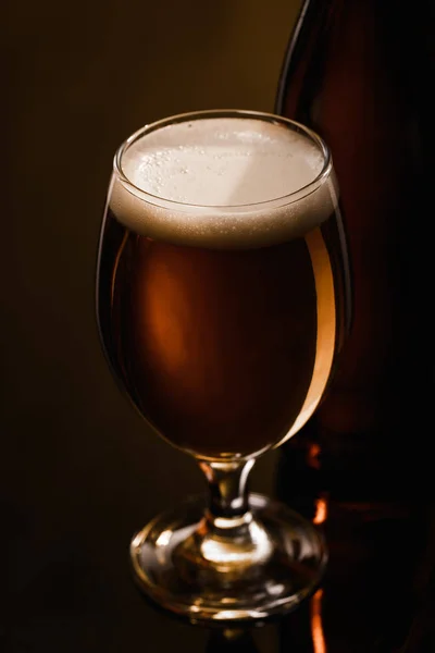 Vista de cerca de la cerveza con espuma blanca en vidrio sobre fondo oscuro con iluminación - foto de stock