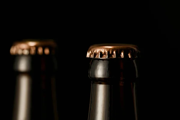 Vista de cerca de botellas de vidrio de cerveza con tapas metálicas aisladas en negro - foto de stock