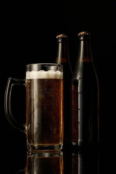 Glas Bier mit Schaum in der Nähe von nassen Flaschen isoliert auf schwarz — Stockfoto