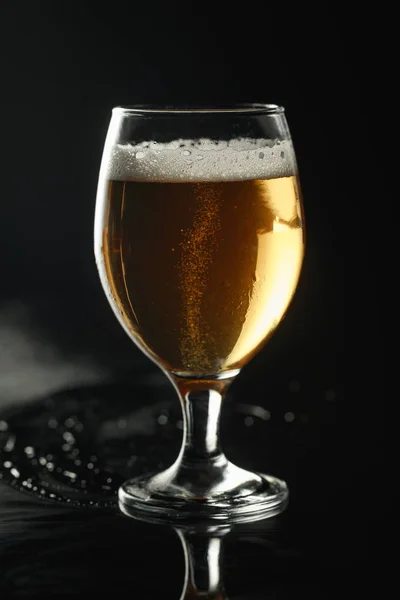 Vaso de cerveza con espuma sobre superficie húmeda aislada sobre negro - foto de stock