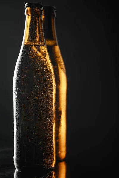 Vista de cerca de botellas mojadas de cerveza con gotas aisladas en negro - foto de stock