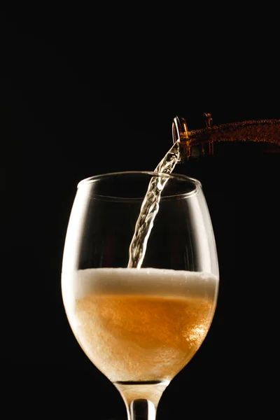 Cerveza dorada que fluye de la botella en vidrio aislado en negro — Stock Photo