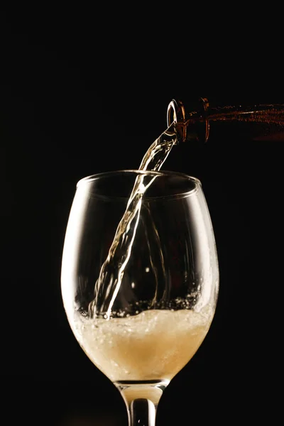 Cerveza que fluye de la botella al vidrio aislado en negro - foto de stock