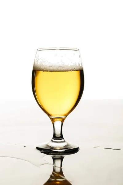 Vaso de cerveza con espuma y charco aislado en blanco - foto de stock