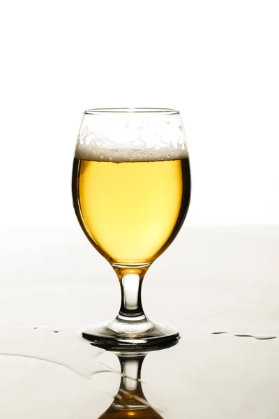 Glass of beer with foam and puddle isolated on white — Stock Photo