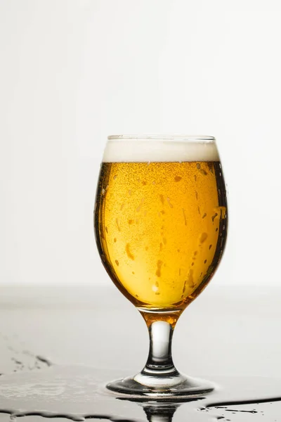 Vaso mojado de cerveza con espuma y charco aislado en blanco - foto de stock