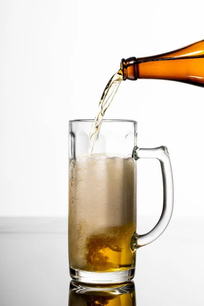 Birra versando da bottiglia in vetro su tavolo isolato su bianco — Foto stock
