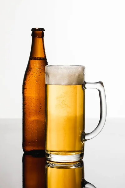 Vetro di birra con schiuma vicino bottiglia bagnata isolato su bianco — Foto stock