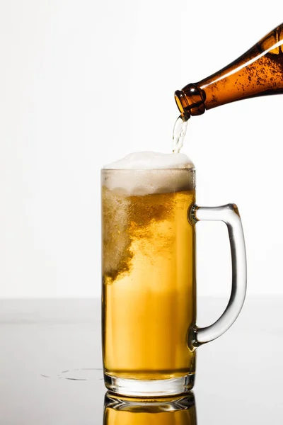 Пиво, що ллється з пляшки в склянку з бульбашками ізольовані на білому — стокове фото