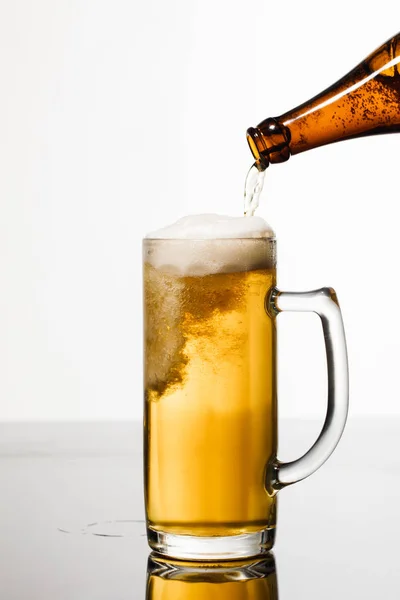 Beer pouring from bottle into glass with bubbles isolated on white — Stock Photo