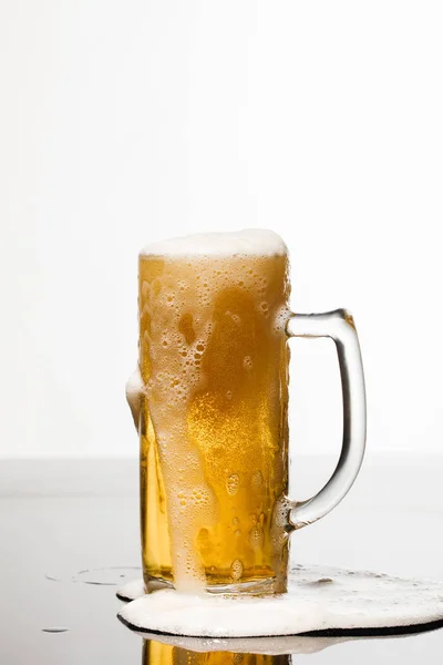 Wet glass of beer with foam and puddle on surface isolated on white — Stock Photo