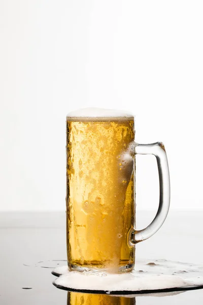 Nassen Glas Bier mit Schaum und verschüttete Pfütze auf Oberfläche isoliert auf weiß — Stockfoto