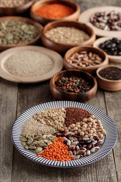 Piatto a strisce con lenticchie, fagioli, ceci, cereali e semi di zucca vicino a ciotole di legno sul tavolo — Foto stock