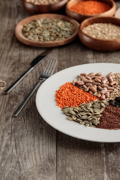 Piatto bianco con lenticchia, semi di zucca e fagioli vicino coltello e forchetta sul tavolo di legno — Foto stock