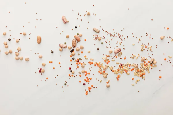 Vue de dessus des haricots épars, lentilles, flocons d'avoine et grains de poivre sur la surface du marbre — Photo de stock