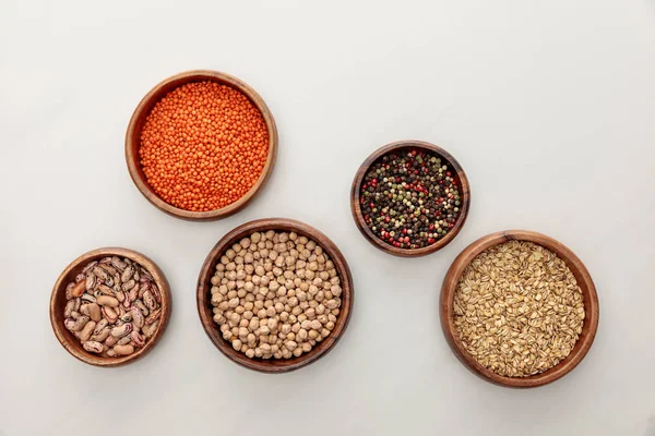 Vista dall'alto di ciotole di legno con lenticchie rosse, fagioli, ceci, farina d'avena e grani di pepe sulla superficie di marmo bianco — Foto stock