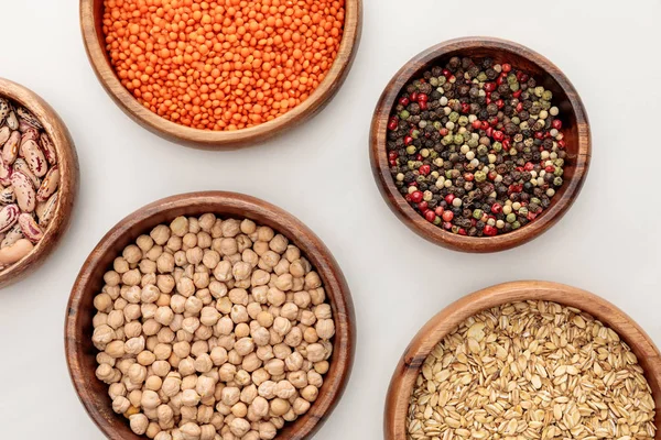 Vue de dessus des bols en bois avec flocons d'avoine, lentilles rouges, grains de poivre et pois chiches sur la surface de marbre blanc — Photo de stock