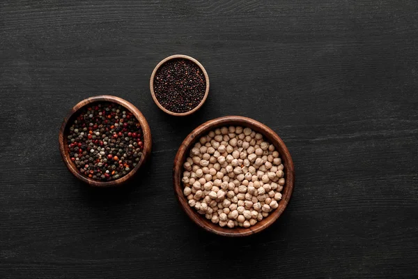 Vista dall'alto su ciotole marroni con grani di pepe, quinoa nera e ceci su superficie di legno scuro — Foto stock