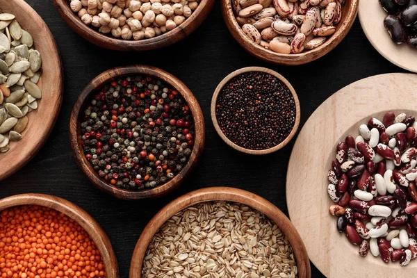 Top view of diverse wooden bowls with uncooked legumes and cereals on dark surface — Stock Photo