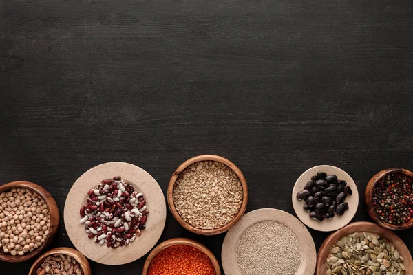 Vista superior de frijoles crudos, cereales, especias y semillas de calabaza en cuencos en superficie de madera oscura con espacio para copiar — Stock Photo