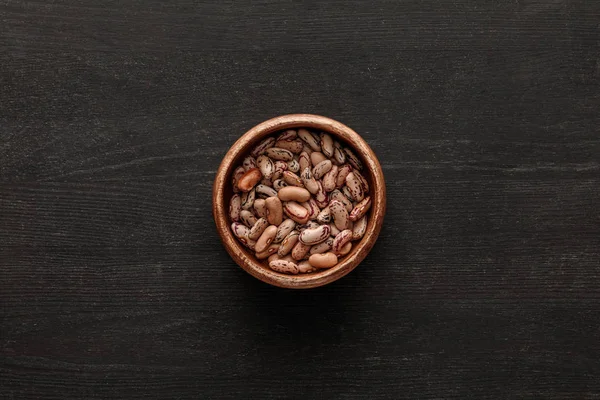 Top view of brown bowl with raw beans on dark wooden surface with copy space — Stock Photo