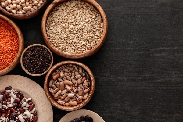 Top view of brown bowls with raw beans, lentil, oatmeals and quinoa on dark wooden surface with copy space — Stock Photo