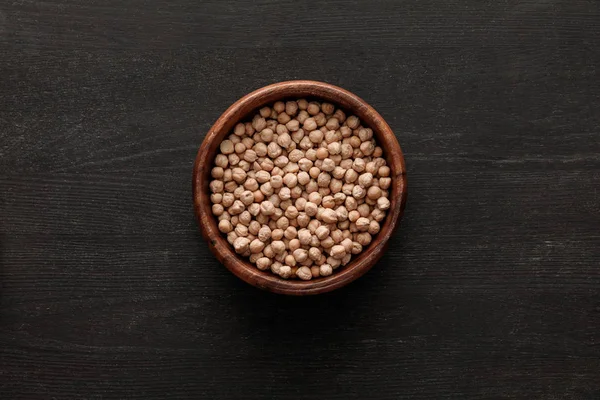 Top view of brown bowl with raw chickpea on dark wooden surface with copy space — Stock Photo