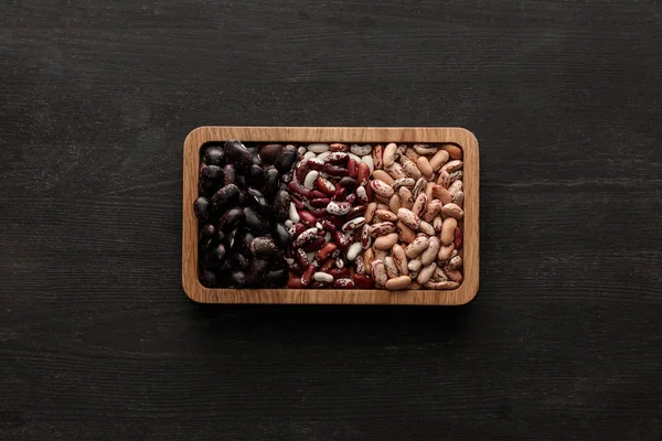 Top view of rectangular brown bowl with raw assorted beans on dark wooden surface with copy space — Stock Photo