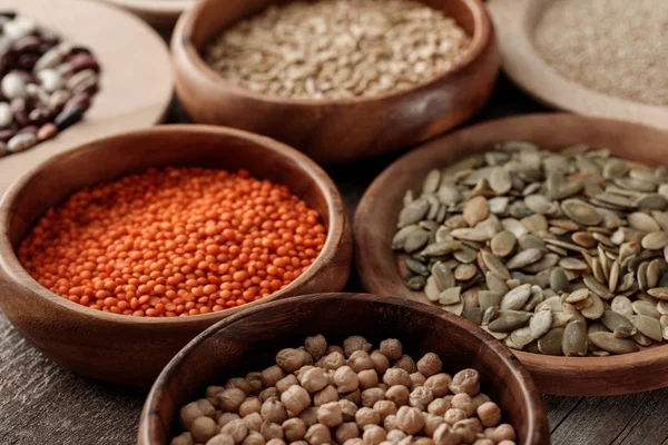 Wooden plates and bowls with raw red lentil, pumpkin seeds and chikpea on table — Stock Photo